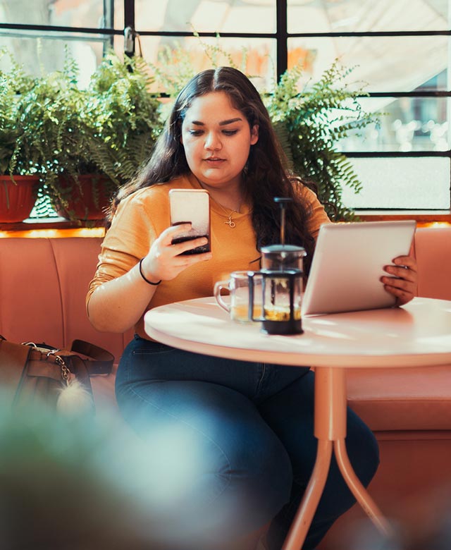 woman using phone and tablet in a cafe