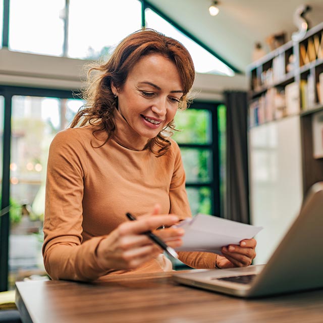 Woman looking at paper in front of her laptop